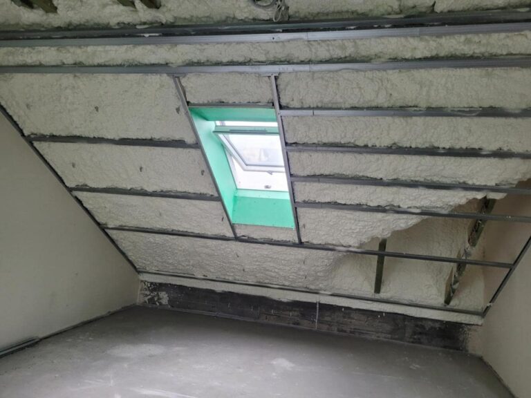 Izolacja poddasza wykonana przy użyciu piany PUR, zapewniająca efektywne ocieplanie przestrzeni. Widoczna konstrukcja dachowa z nowoczesnym materiałem izolacyjnym, który zwiększa komfort termiczny w domu.