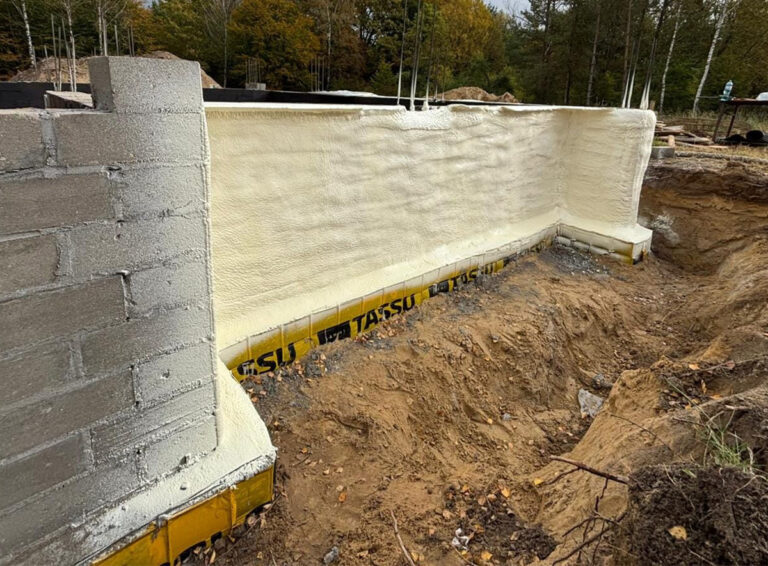 Izolacja fundamentów budynku wykonana przy użyciu piany PUR, ukazująca proces ocieplania, który poprawia efektywność energetyczną domu. Widoczne warstwy materiału izolacyjnego na etapie budowy.